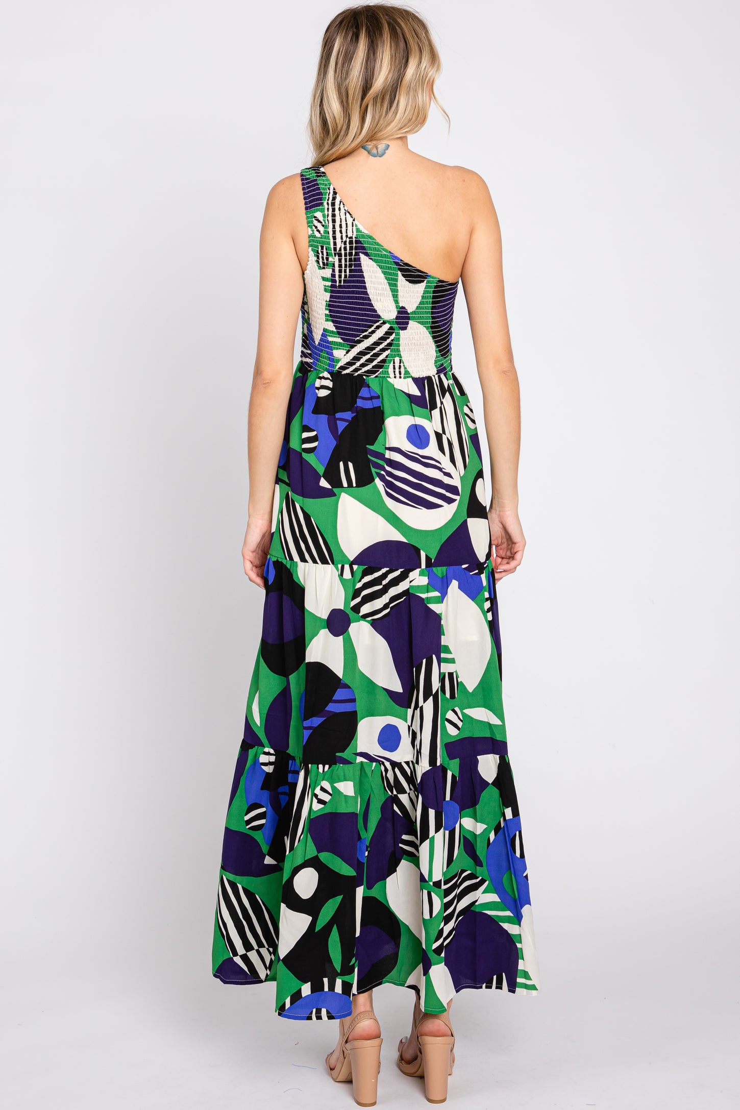 woman wearing a colorful patterned one-shoulder maxi dress with a tiered skirt and a fitted bodice