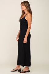 woman wearing a black spaghetti strap maxi dress and black sandals, standing in profile against a neutral background