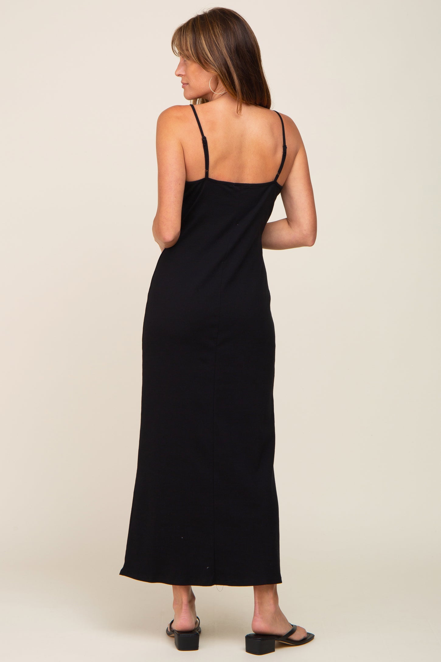 woman wearing a fitted black maxi dress with thin straps, showing the back view