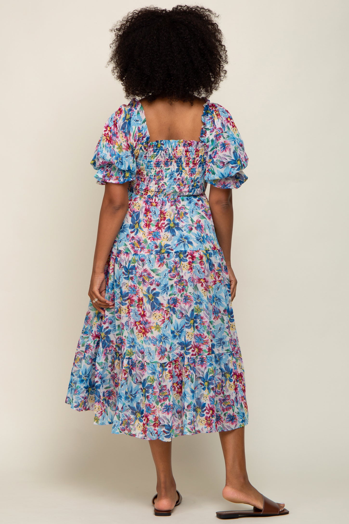 woman wearing a blue floral maxi dress with puff sleeves and a tiered skirt, seen from the back