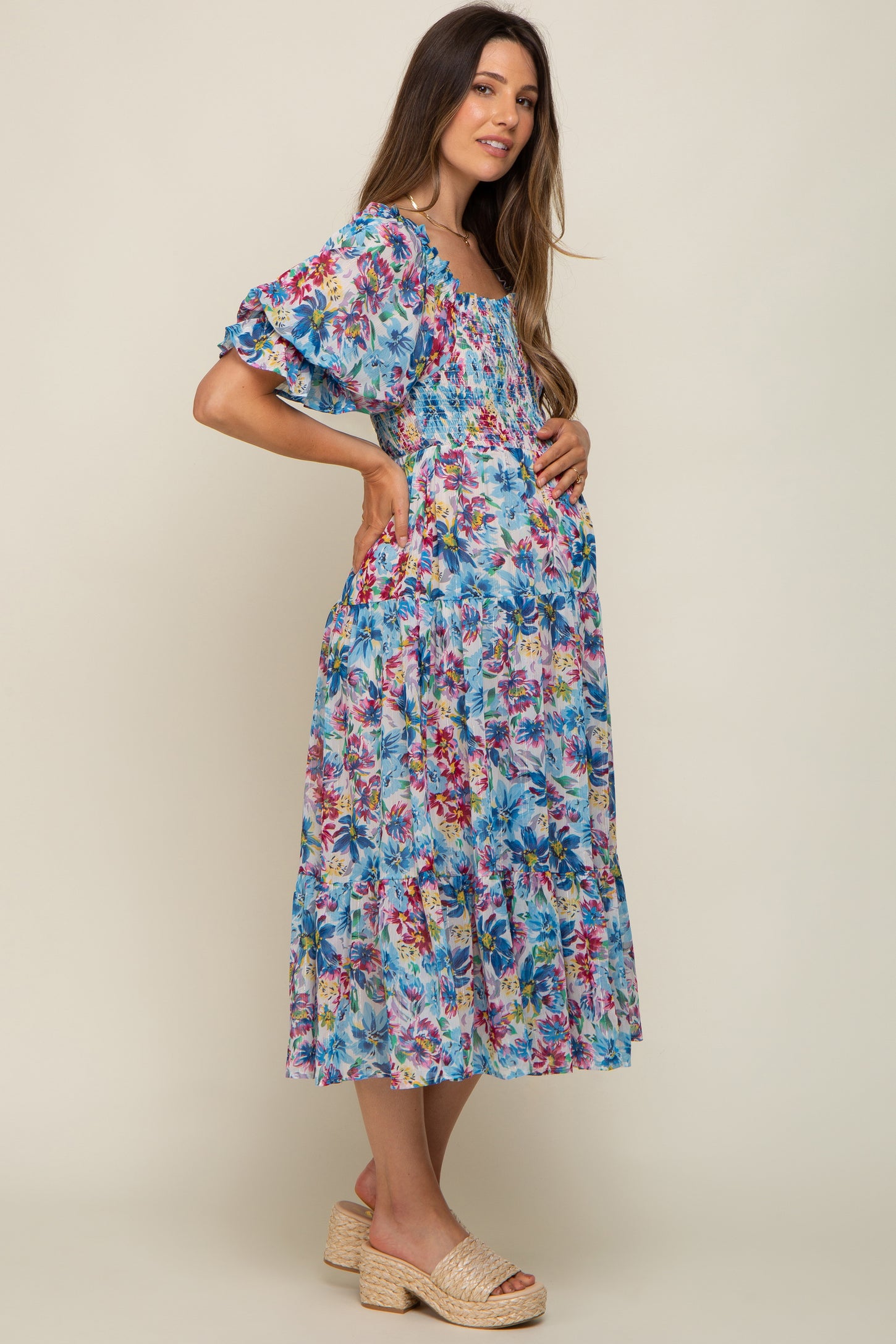 woman wearing a floral blue maternity dress with puff sleeves and holding her baby bump