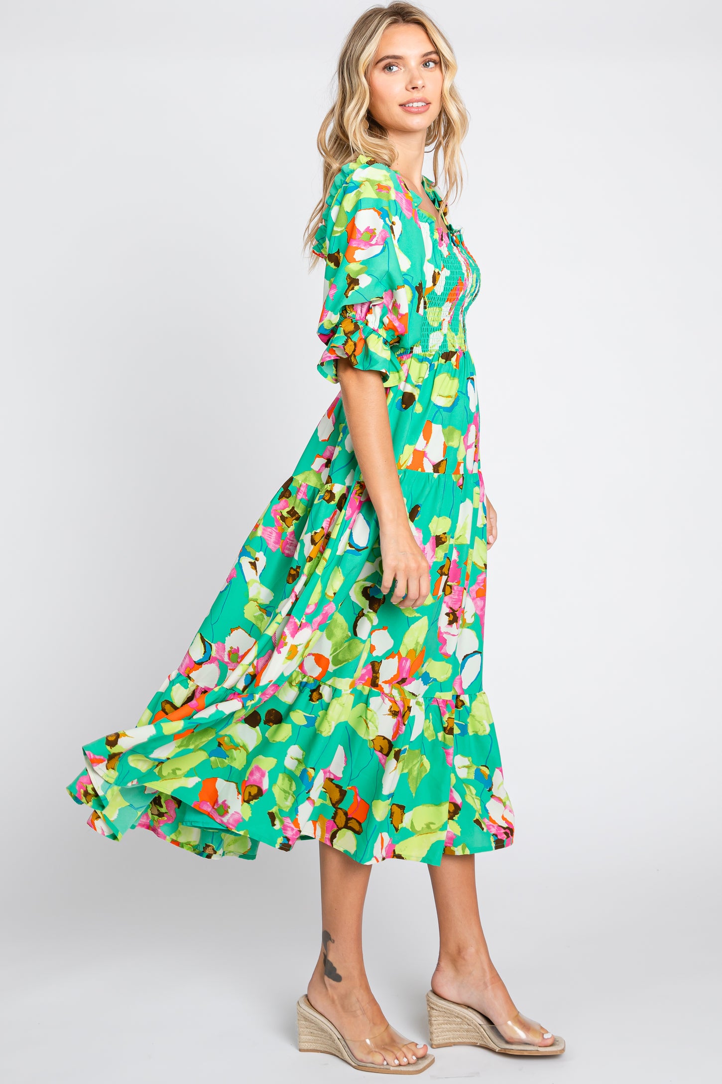 woman wearing a green floral maxi dress with puff sleeves and a tiered skirt, standing and smiling