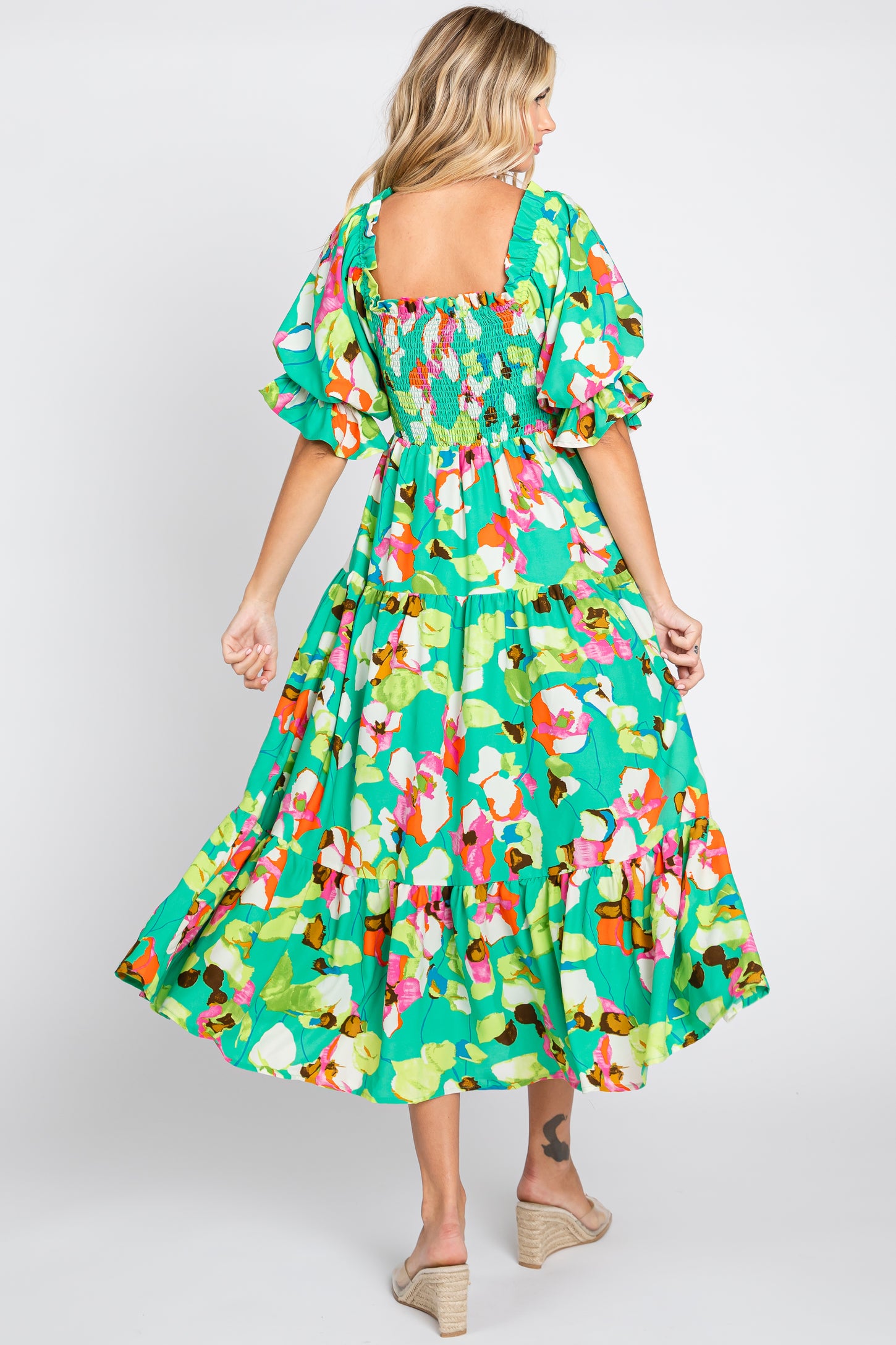 woman wearing a vibrant floral maxi dress with puff sleeves and a smocked back, seen from the back, standing in a twirl