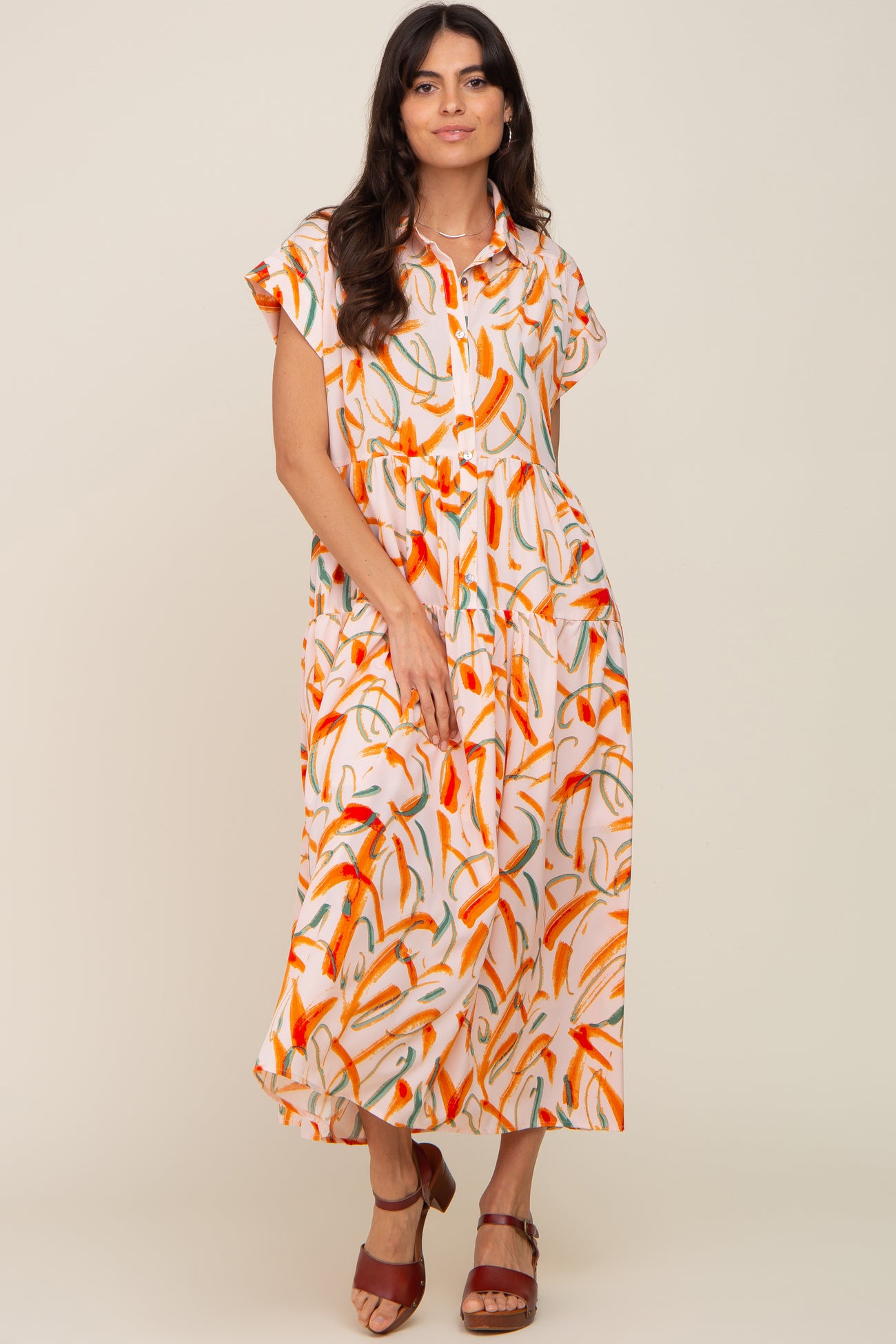 woman wearing a short sleeve tiered midi dress with orange and green abstract print and brown sandals