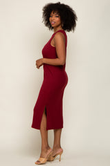 woman with curly hair wearing a sleeveless burgundy midi dress with a side slit and tan heels