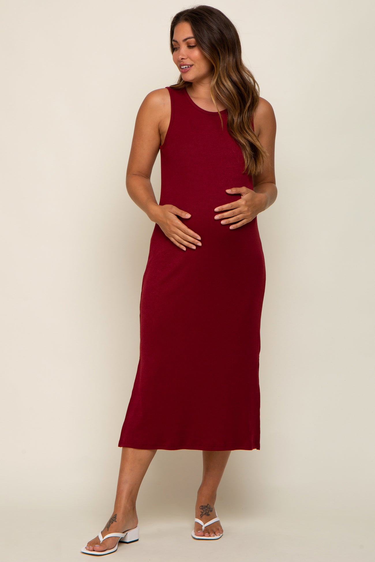 woman wearing a burgundy sleeveless maternity dress and cradling her baby bump