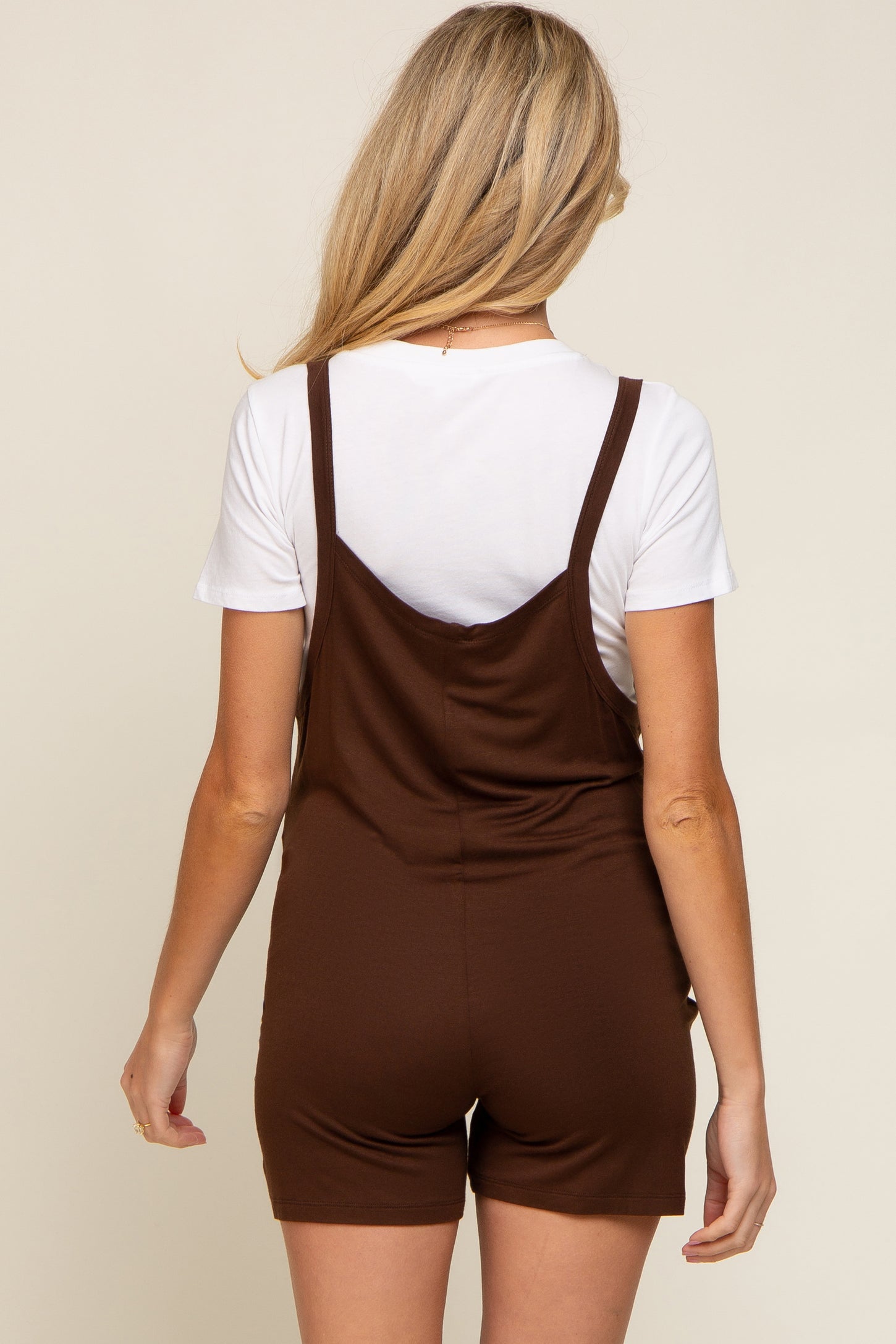Back view of a woman wearing a brown sleeveless romper over a white short-sleeve t-shirt