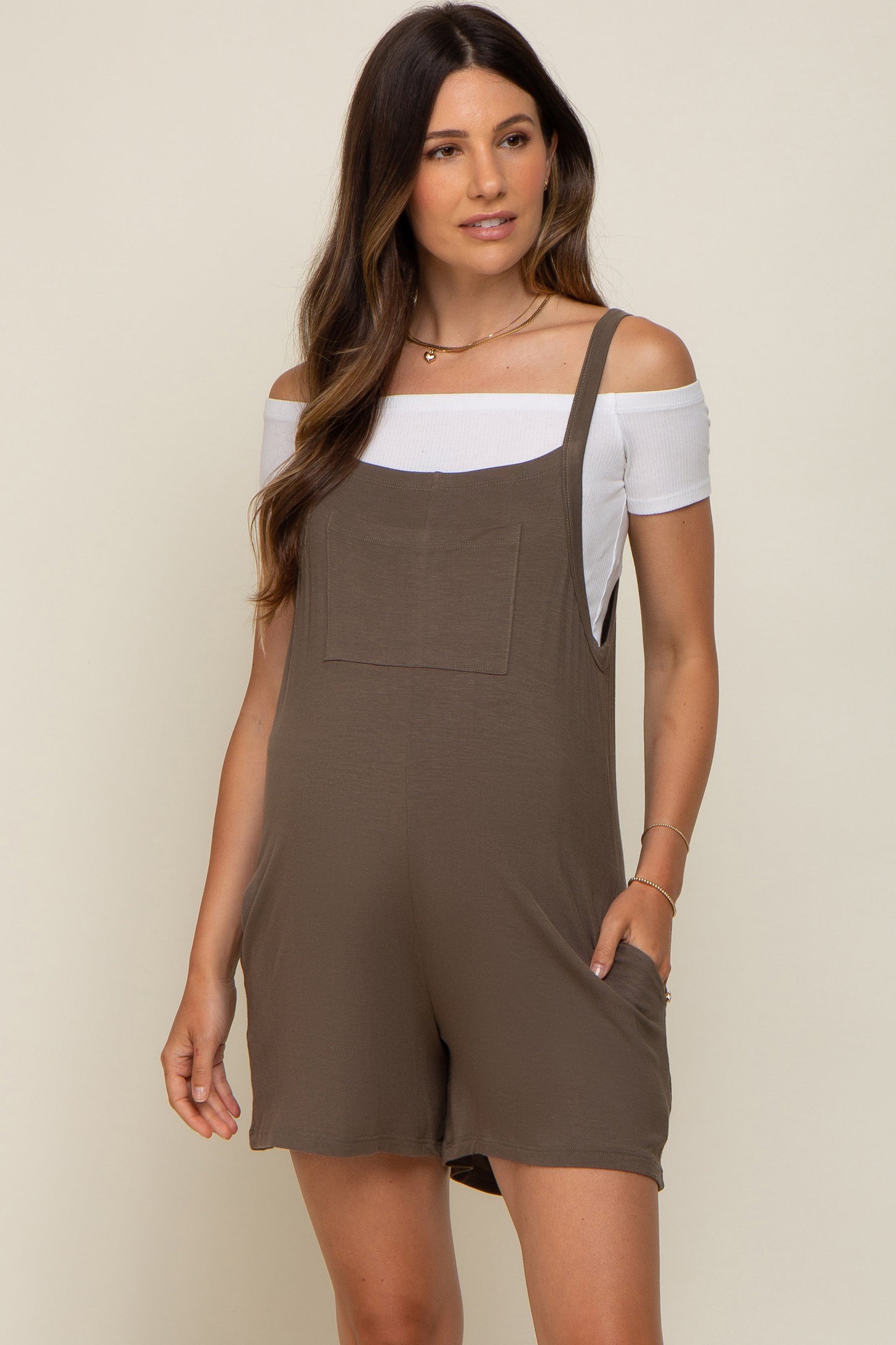 pregnant woman wearing olive green maternity romper over a white off-the-shoulder top