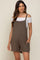 pregnant woman wearing olive green maternity romper over a white off-the-shoulder top