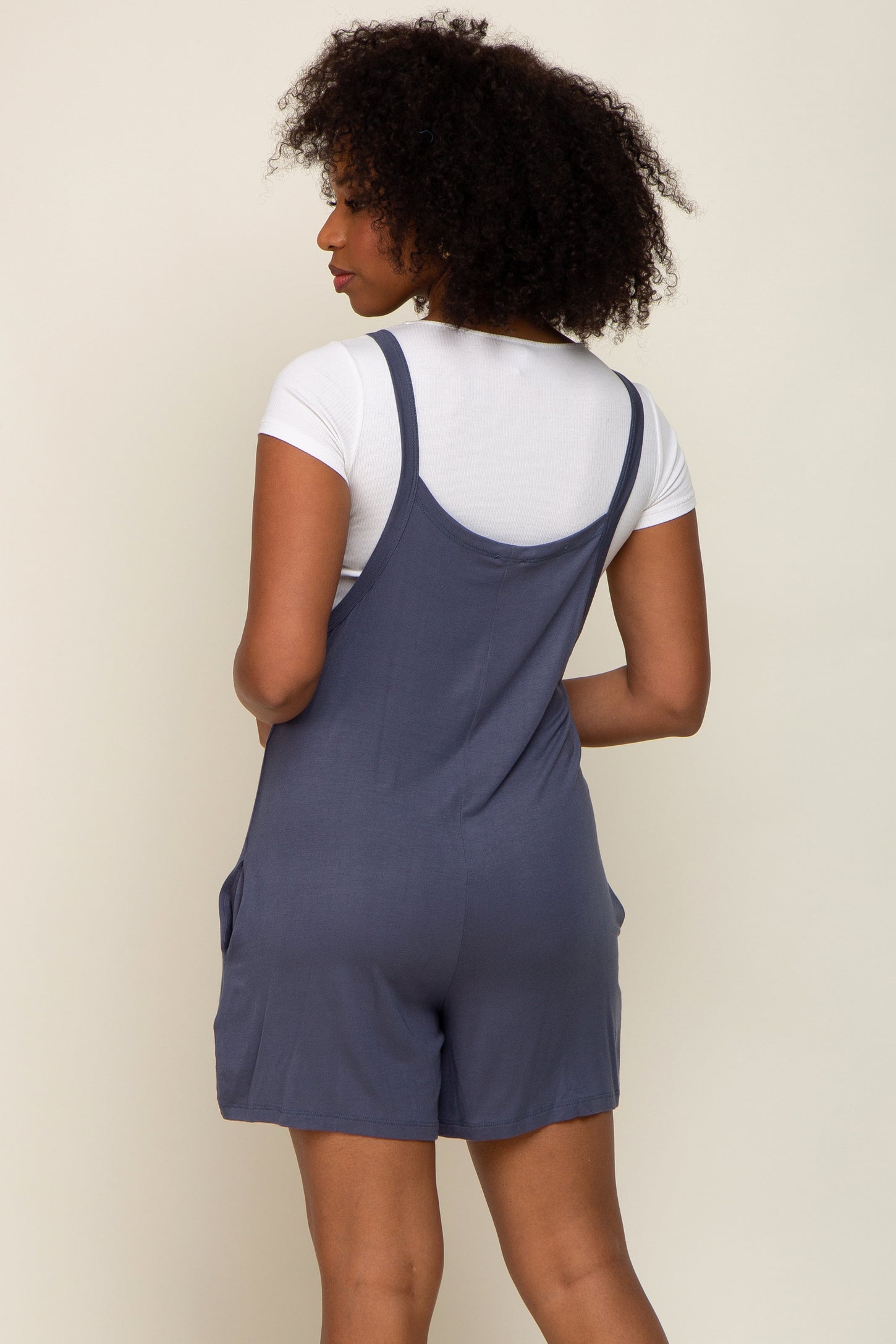 woman wearing a navy blue romper with adjustable straps and side pockets, viewed from the back