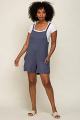 woman with curly hair wearing a blue maternity romper over a white t-shirt and woven sandals