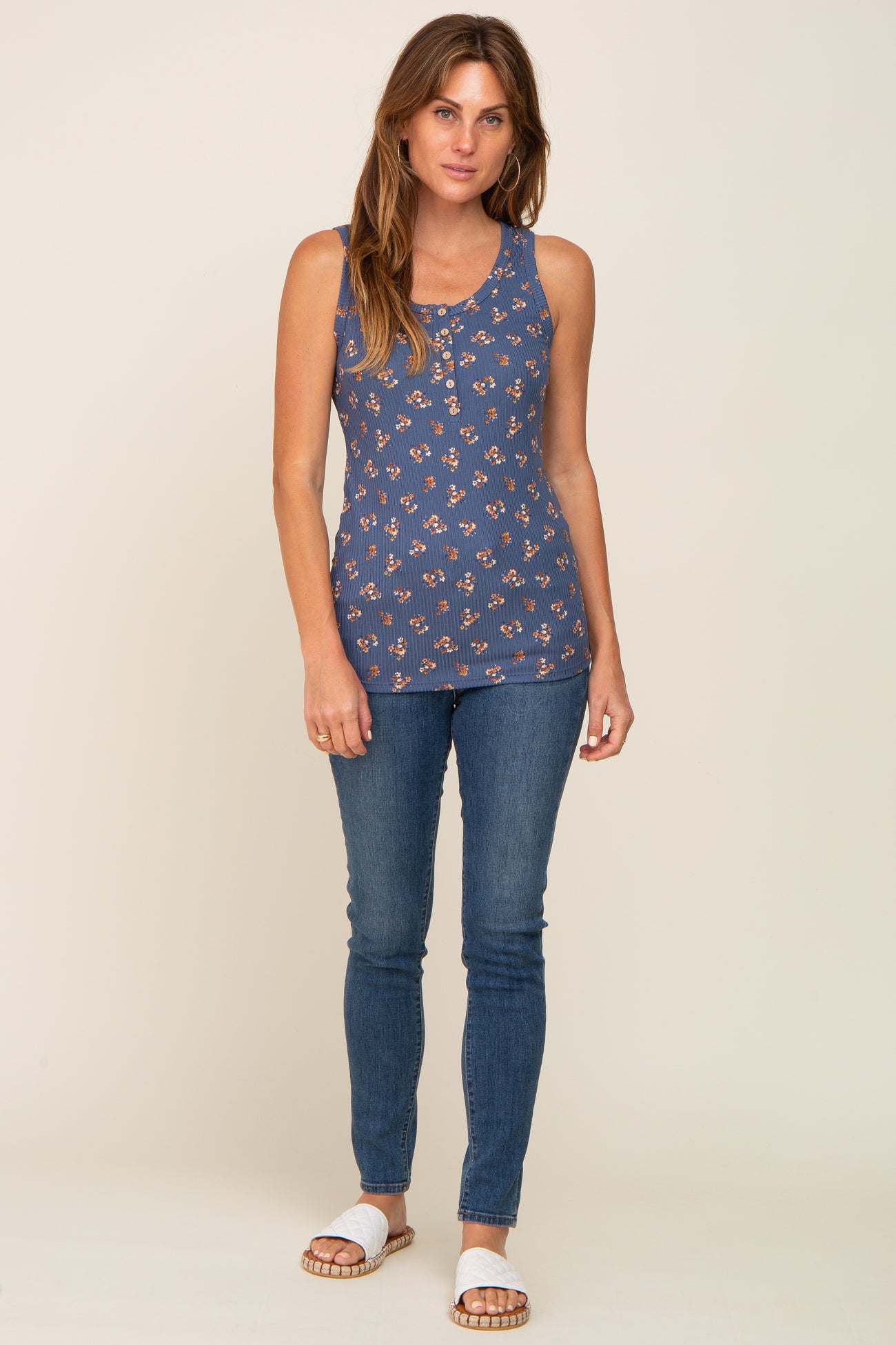 woman wearing blue floral print sleeveless henley top and skinny jeans with white slide sandals