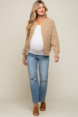 pregnant woman wearing a tan cable knit cardigan, white maternity top, and distressed blue jeans