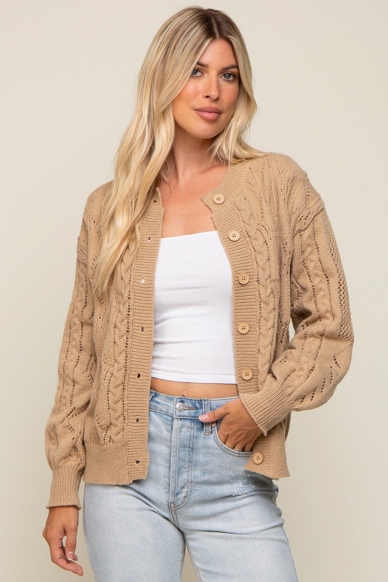 woman wearing a tan cable knit cardigan sweater over a white top and light wash denim jeans