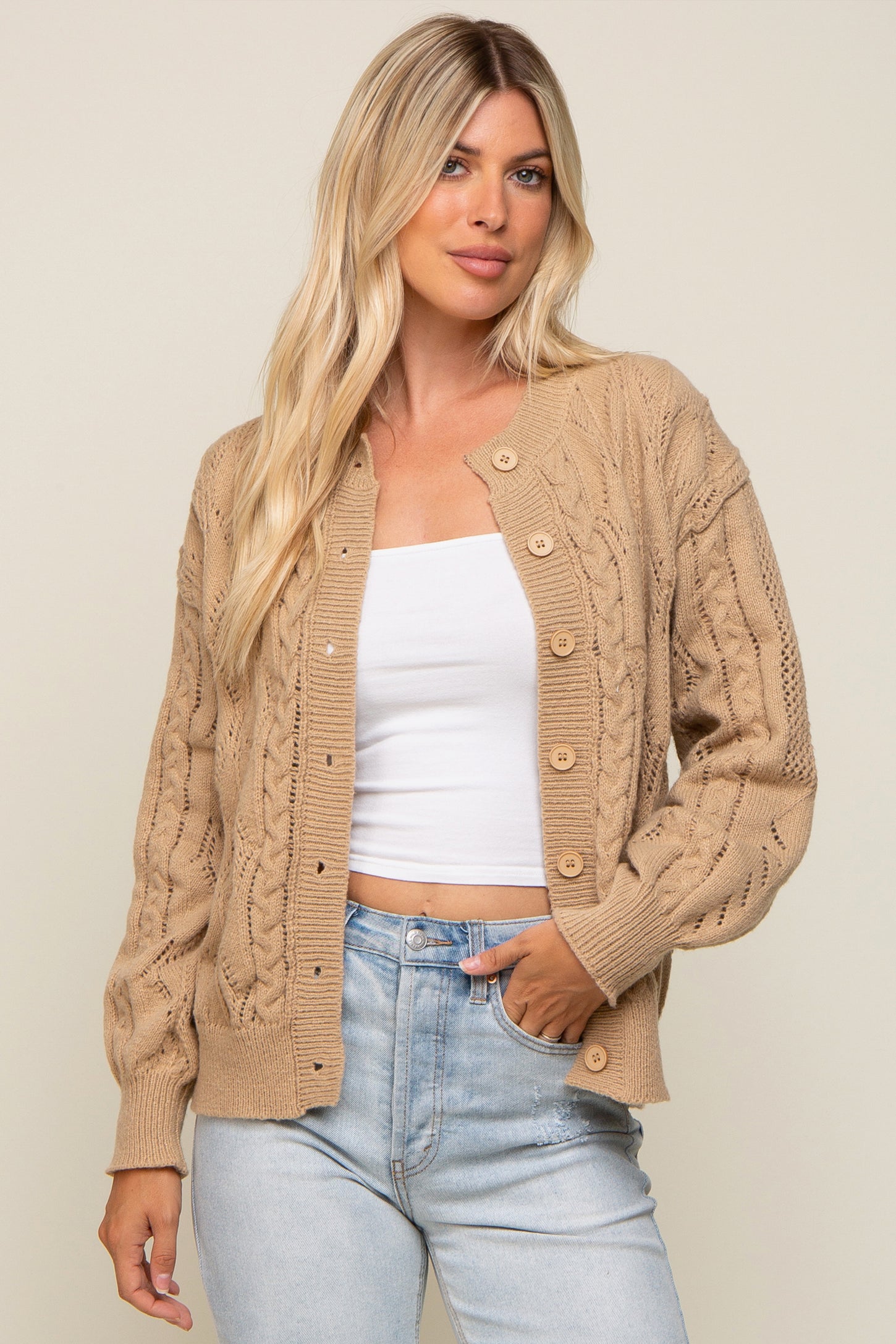 woman wearing a tan cable knit cardigan sweater over a white top and light wash denim jeans