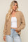 woman wearing a tan cable knit cardigan sweater over a white top and light wash denim jeans