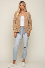 Woman wearing a tan cable knit cardigan, white crop top, and light wash distressed jeans