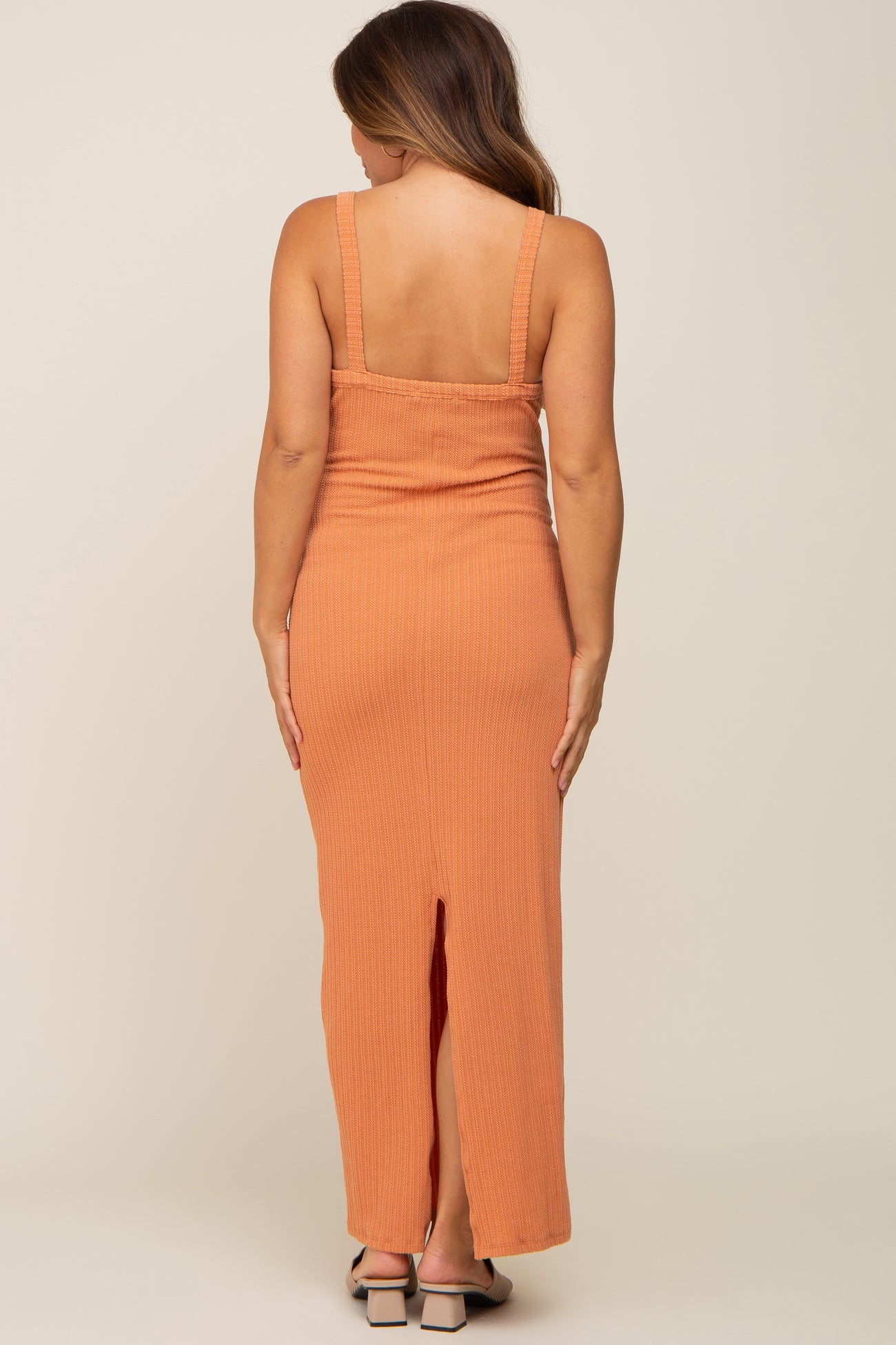 Back view of a woman wearing a long orange ribbed knit maxi dress with a back slit and square neckline