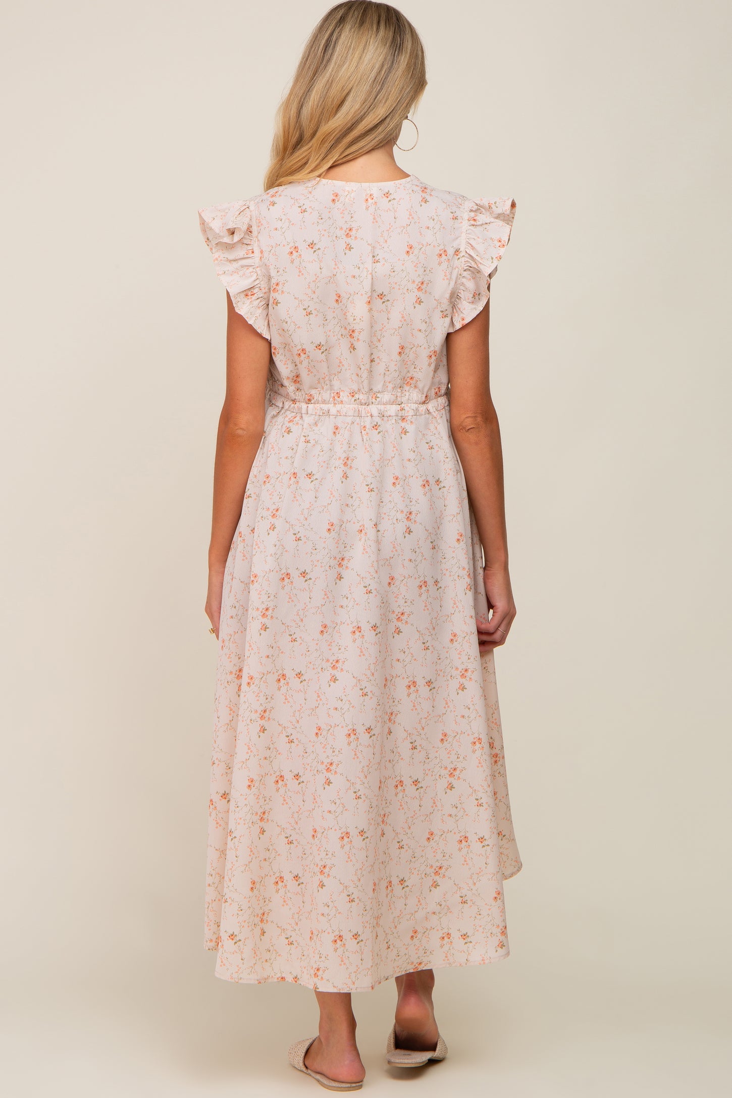 Back view of woman wearing a cream floral midi dress with ruffle sleeves and elastic waist