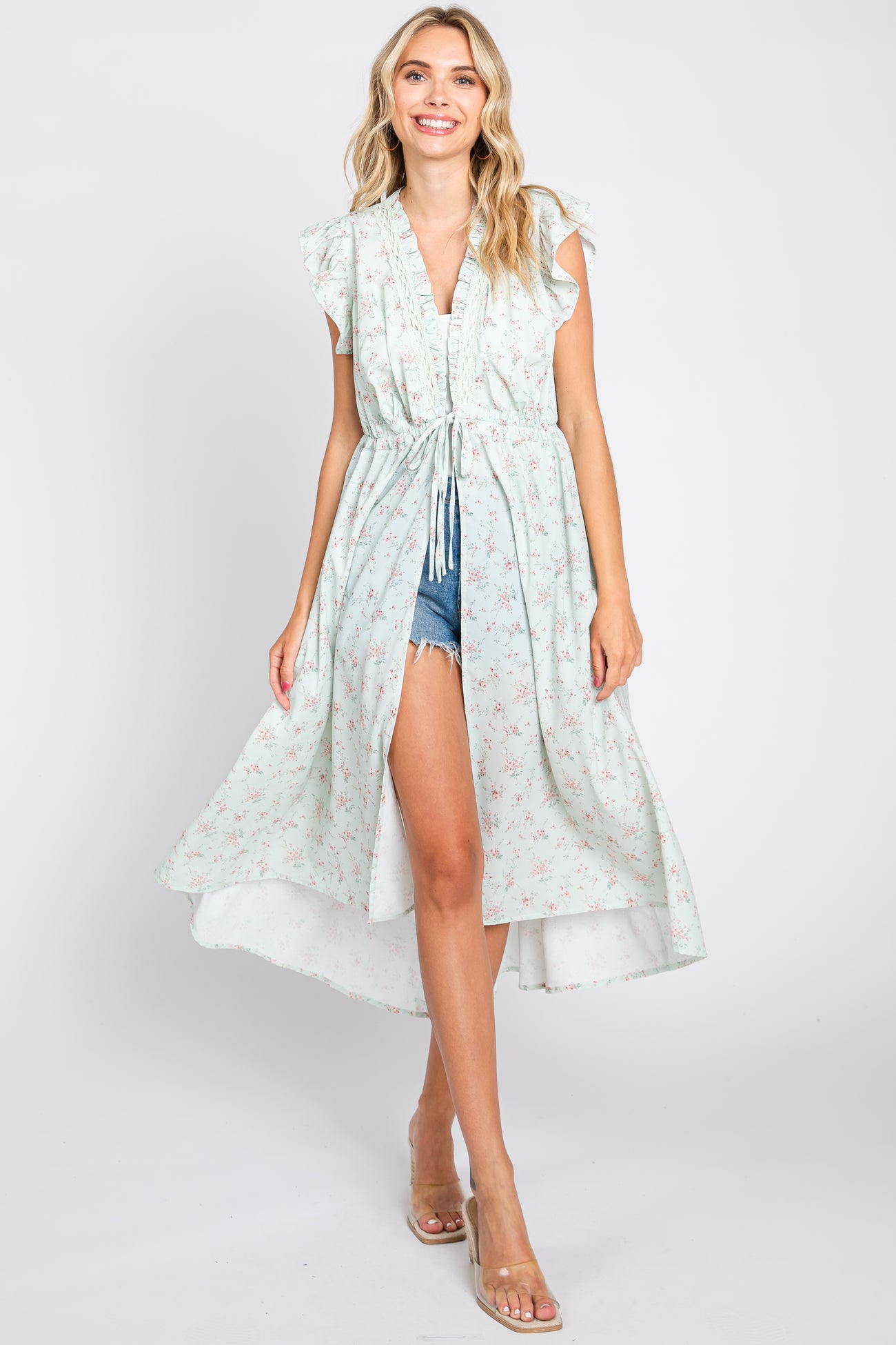 woman wearing a mint green floral print ruffle sleeve kimono over denim shorts and a white top