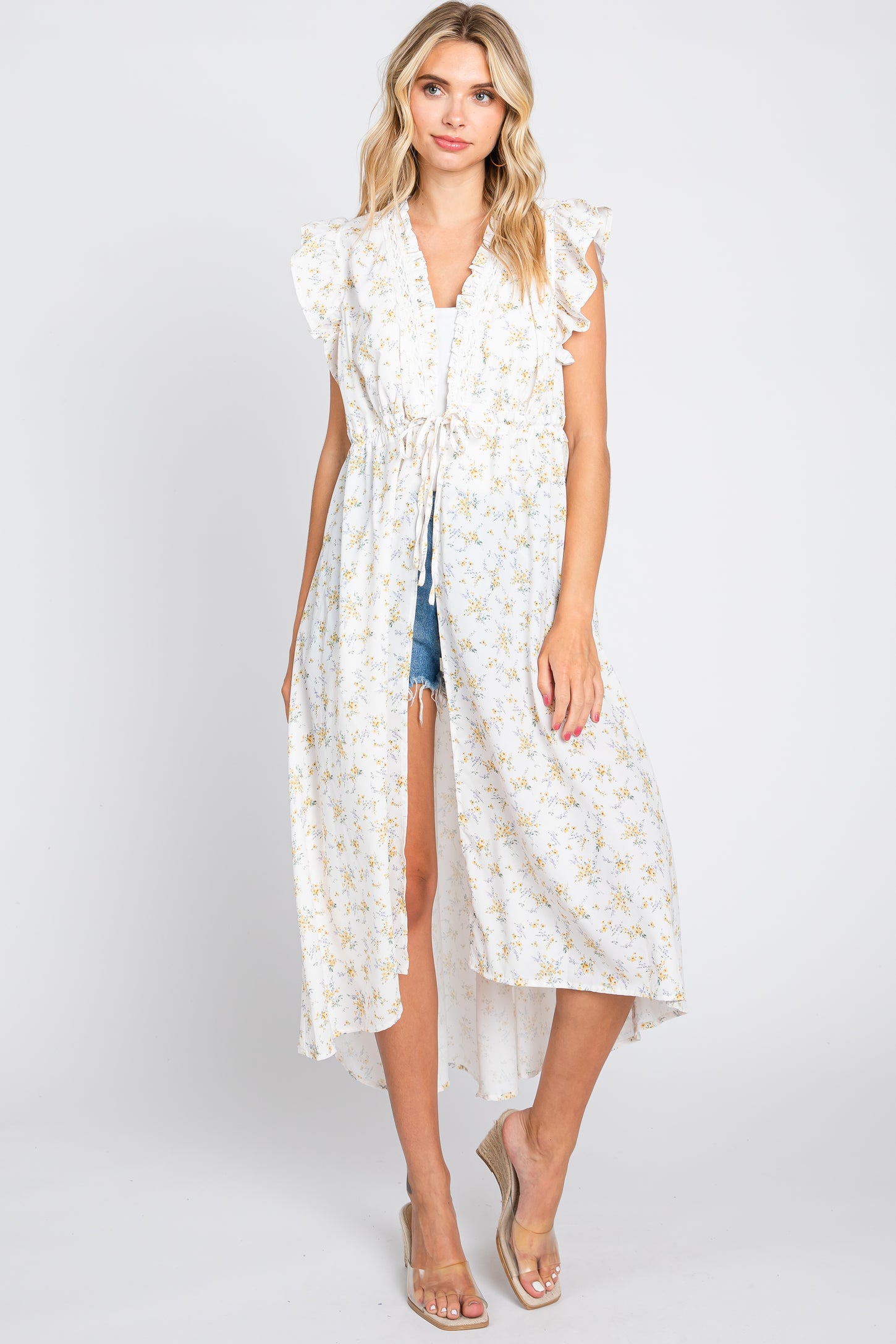 woman wearing a white floral print long kimono with ruffle sleeves over denim shorts and wedge sandals