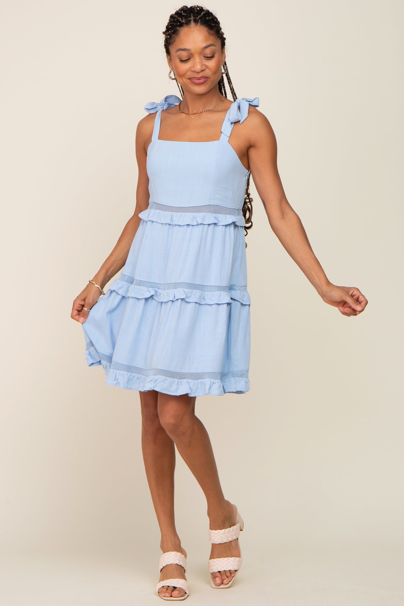 Woman wearing a light blue sleeveless tiered mini dress with bow straps and mesh lace detailing