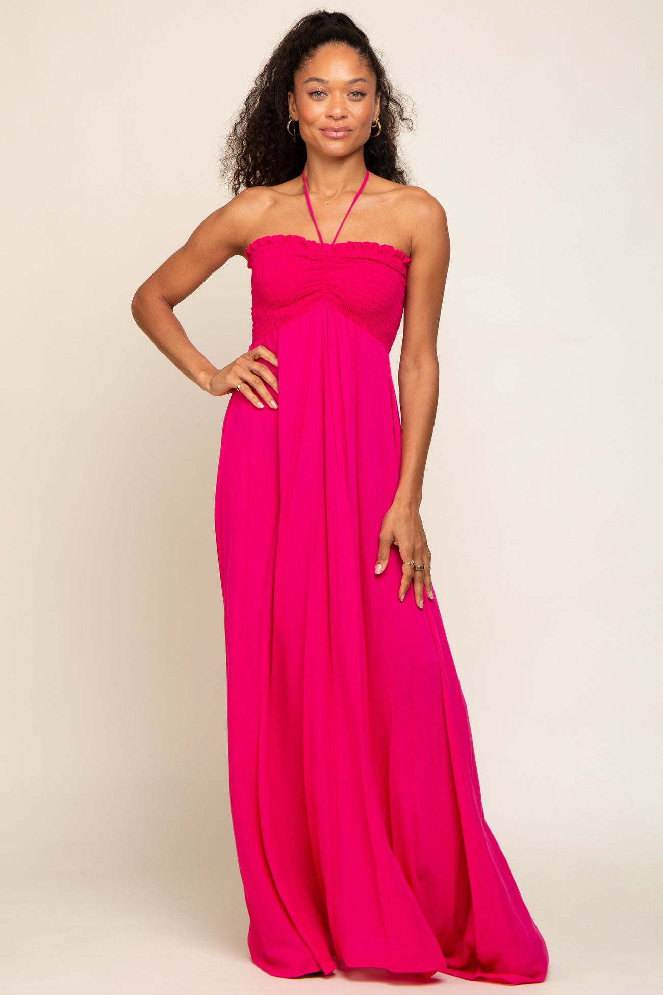 Woman wearing a hot pink halter neck maxi dress with a smocked bodice and flowy skirt