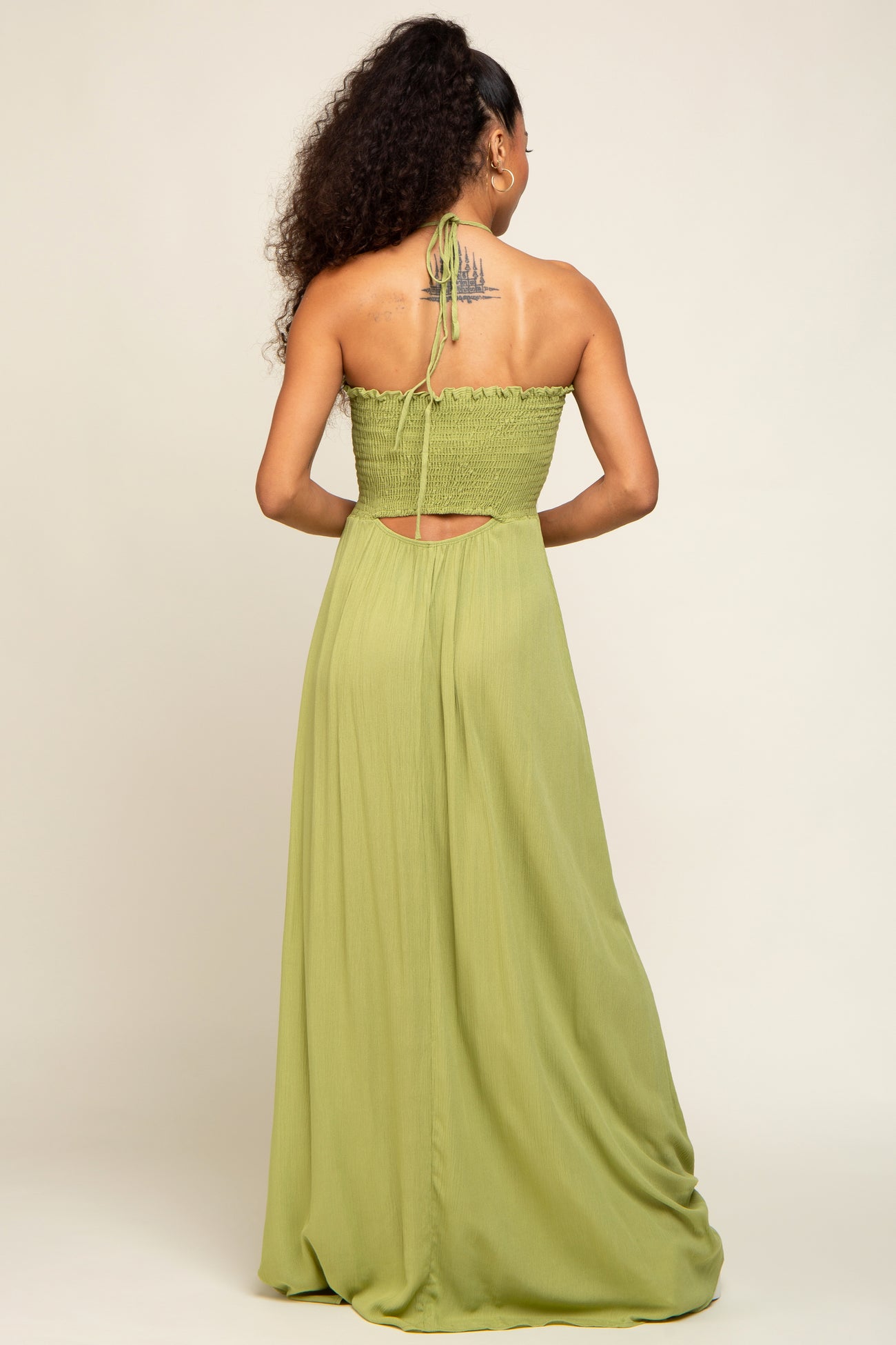 Back view of a woman wearing a sage green smocked maxi dress with a halter tie and back cutout