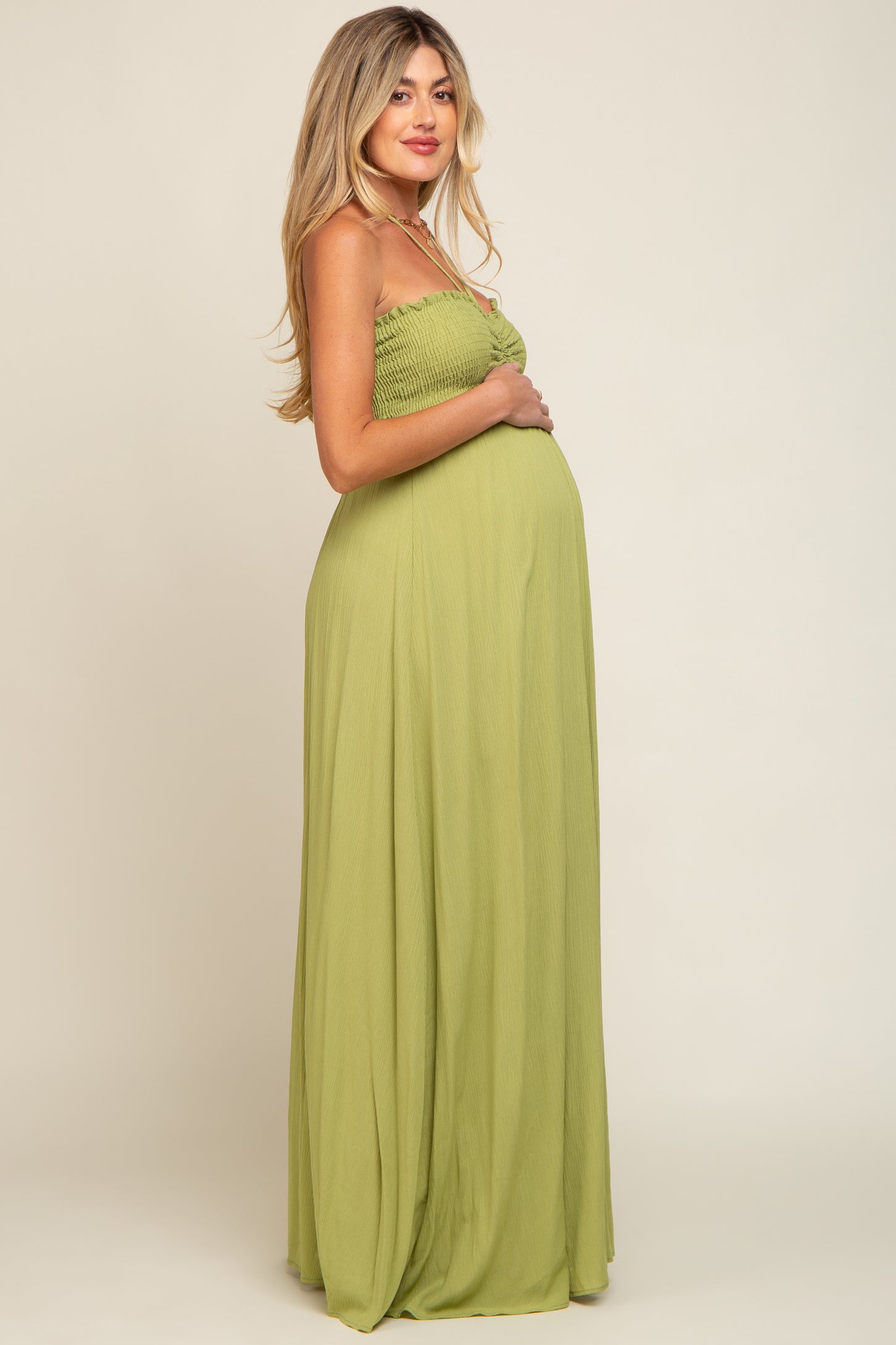 pregnant woman in a sage green smocked maternity maxi dress posing against a neutral background