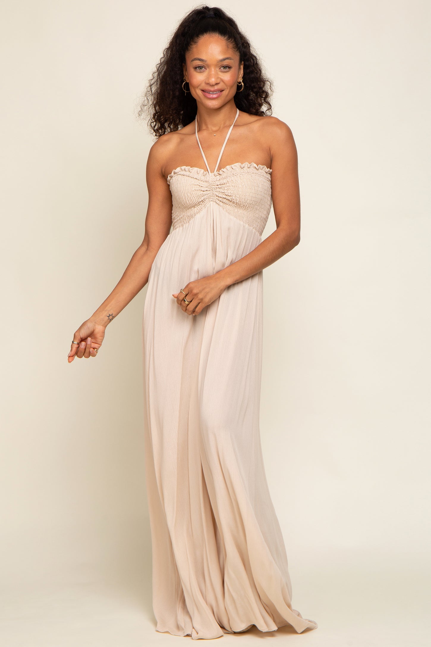 woman wearing a strapless nude-colored maxi dress with gathered detailing around the bust and flowing skirt