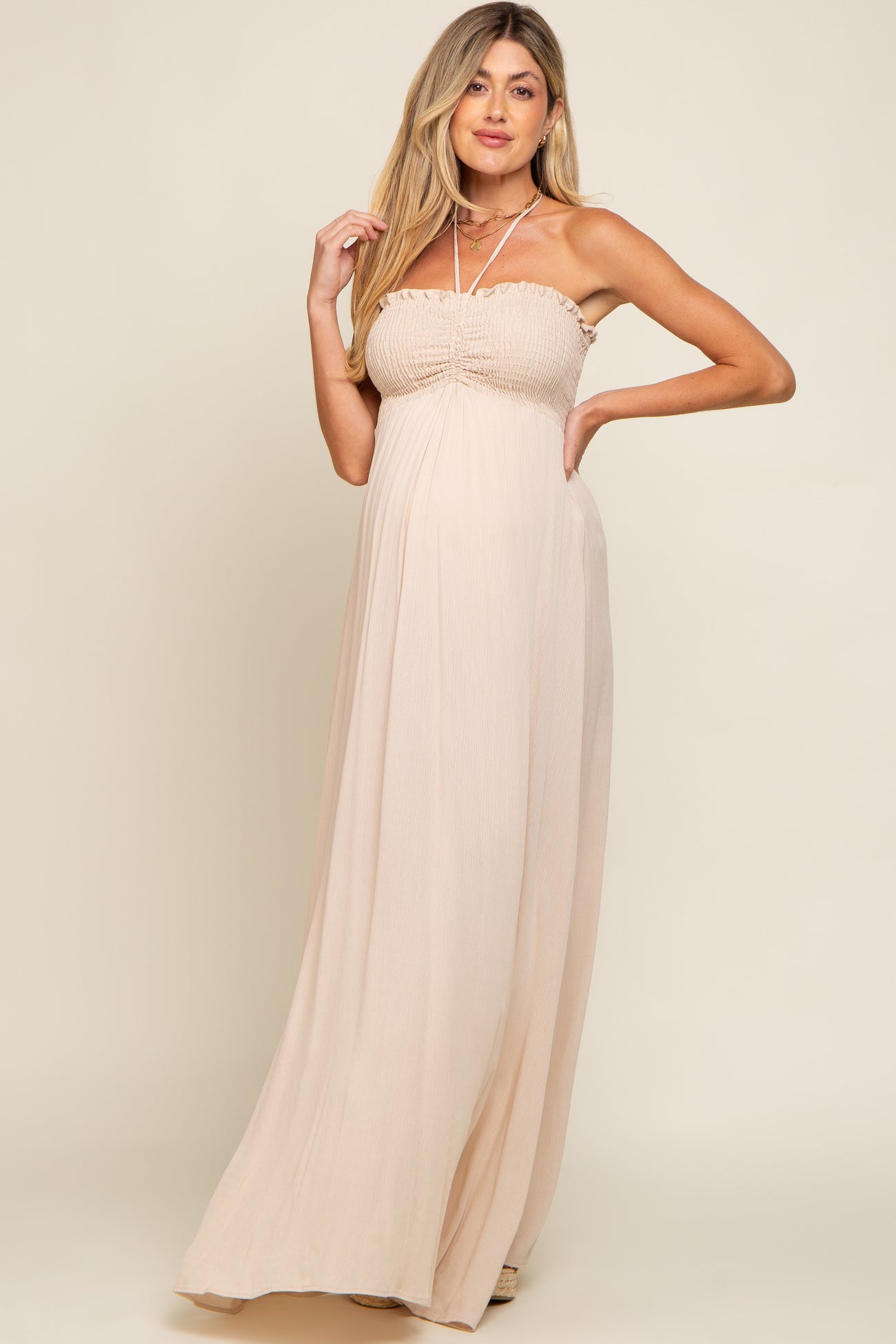 woman wearing a light beige strapless maternity maxi dress with a smocked bodice and flowing skirt, showcasing her baby bump