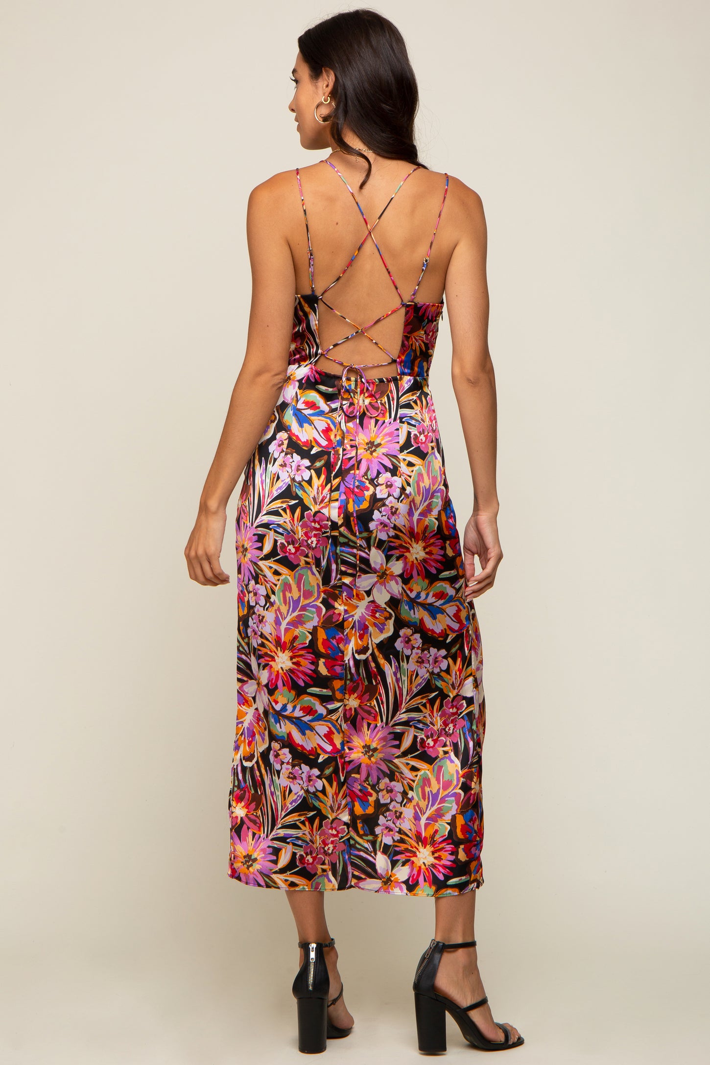 Woman wearing a floral midi dress with a lace-up open back and black high heel sandals
