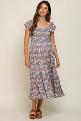 woman wearing a blue floral smocked maternity midi dress with flutter sleeves and brown sandals