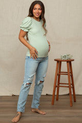 woman wearing a light green maternity top with puff sleeves and distressed blue jeans, showing her baby bump