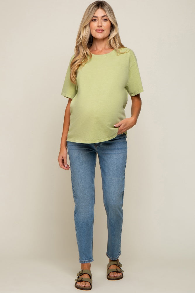 woman wearing a light green maternity top and blue skinny jeans, showing her baby bump