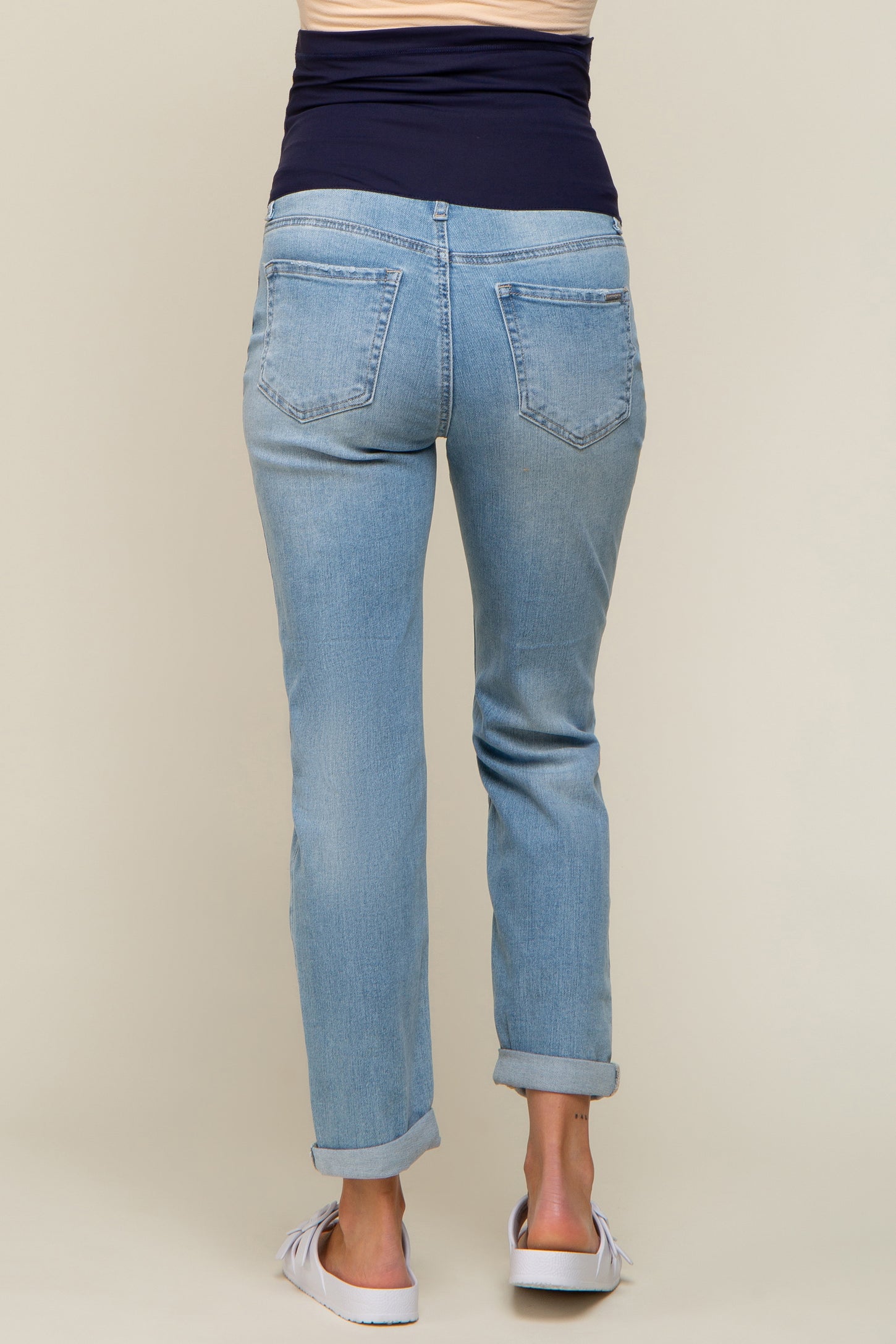 woman wearing light blue maternity jeans with a folded hem and a dark blue top, showing her baby bump from behind