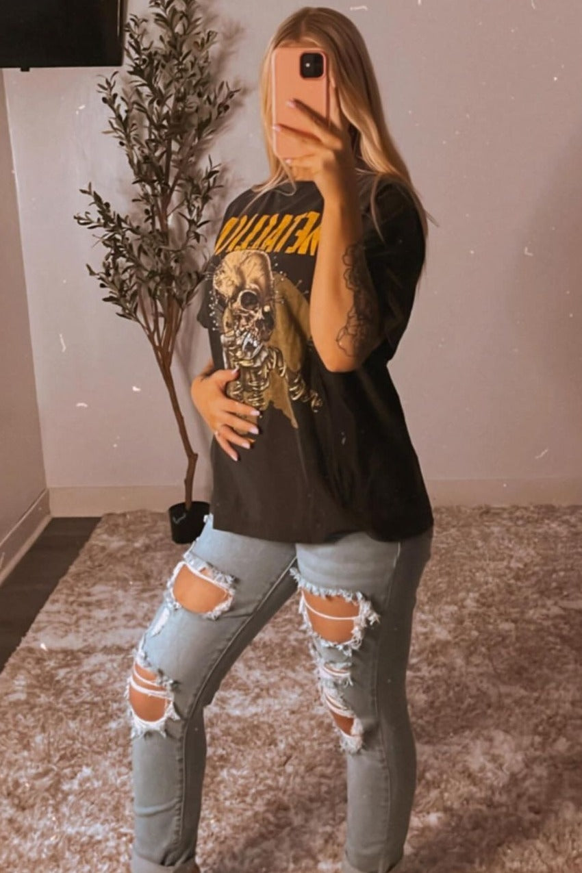 woman wearing a distressed black graphic t-shirt and light blue ripped maternity jeans, holding her baby bump