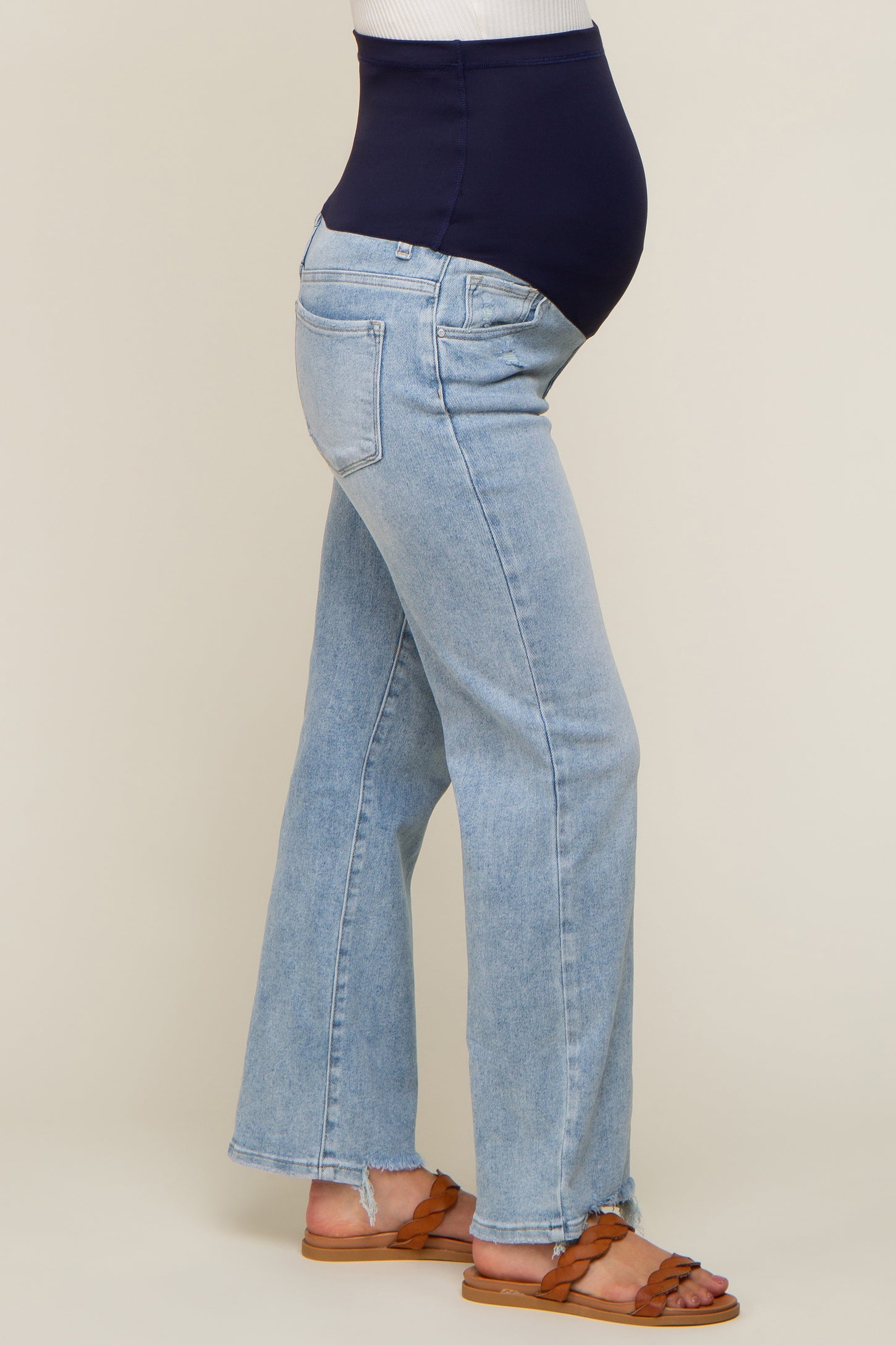 pregnant woman wearing light wash maternity flare jeans with a navy blue belly band and brown sandals