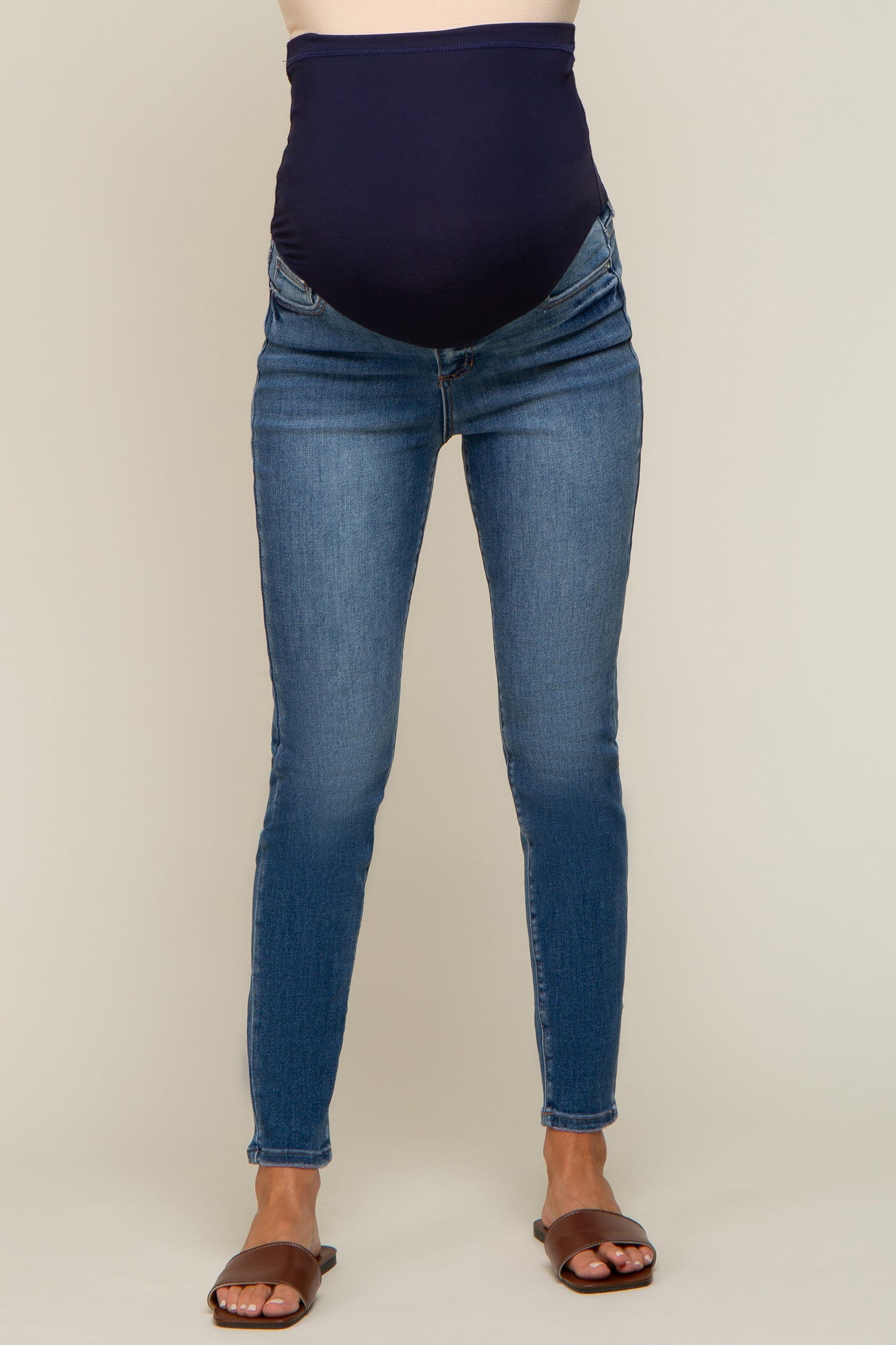 person wearing blue maternity skinny jeans with a navy over-the-belly support band and brown sandals