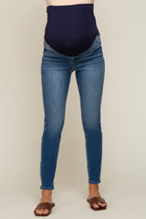 person wearing blue maternity skinny jeans with a navy over-the-belly support band and brown sandals