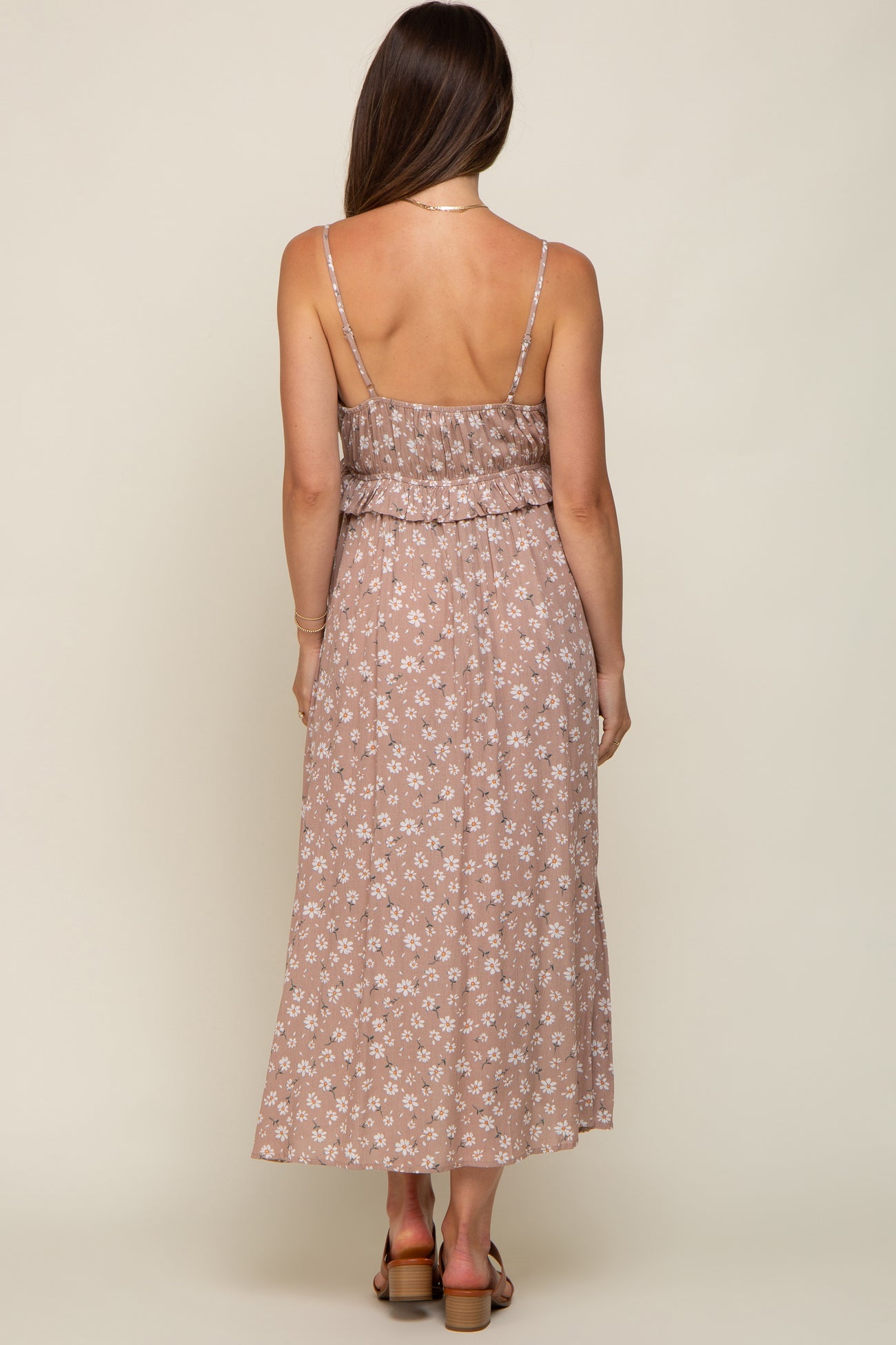 Back view of a woman wearing a mauve floral print maxi dress with spaghetti straps and ruffle detail