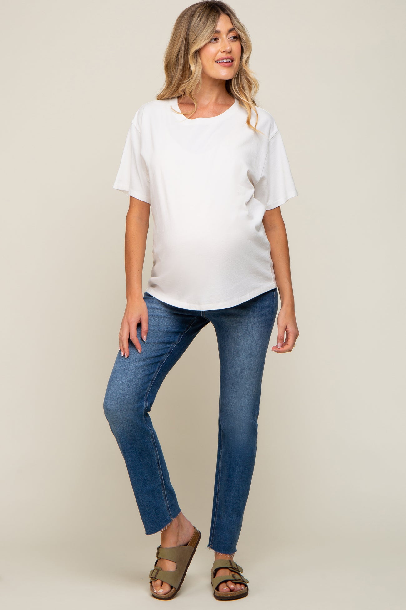 woman wearing a white short sleeve maternity top and blue skinny jeans, showing her baby bump