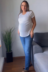 woman wearing a white short sleeve maternity top and blue skinny jeans, showing her baby bump