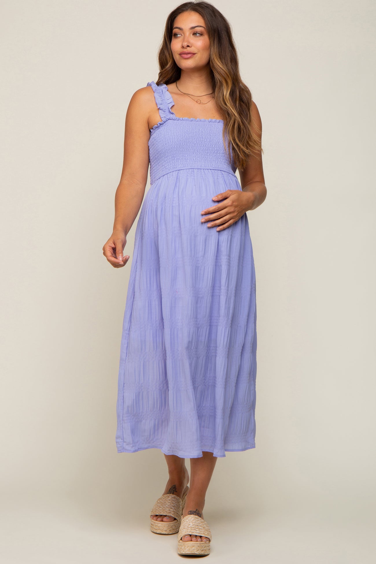Pregnant woman wearing a light purple smocked maternity midi dress with ruffle straps and woven platform sandals