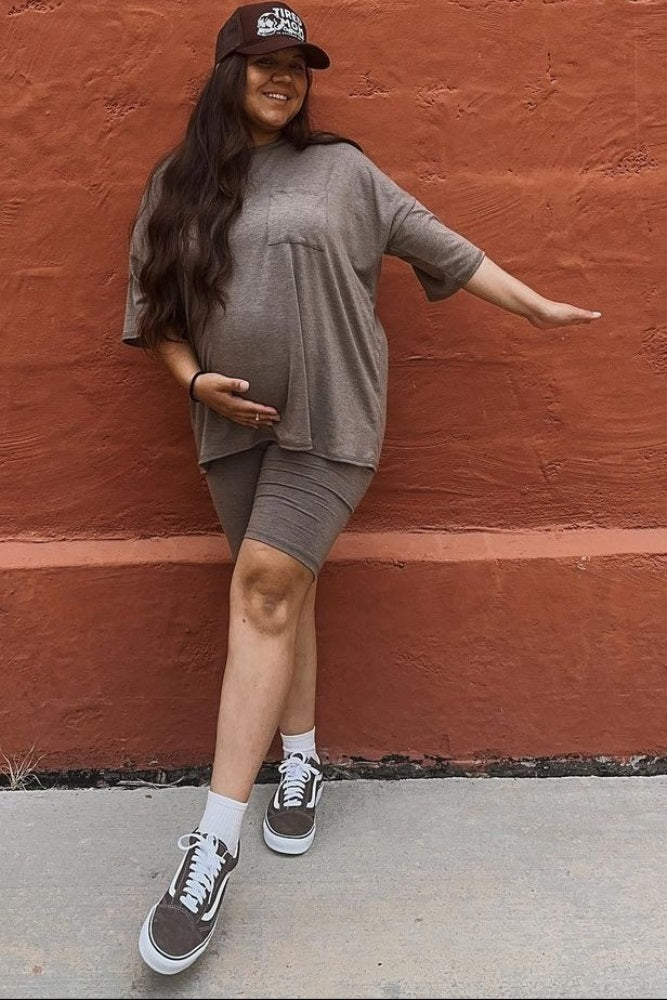 woman wearing a brown maternity oversized top and matching bike shorts, posing with a visible baby bump