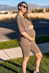 woman wearing a brown maternity outfit consisting of a loose top and bike shorts, showing her baby bump outdoors