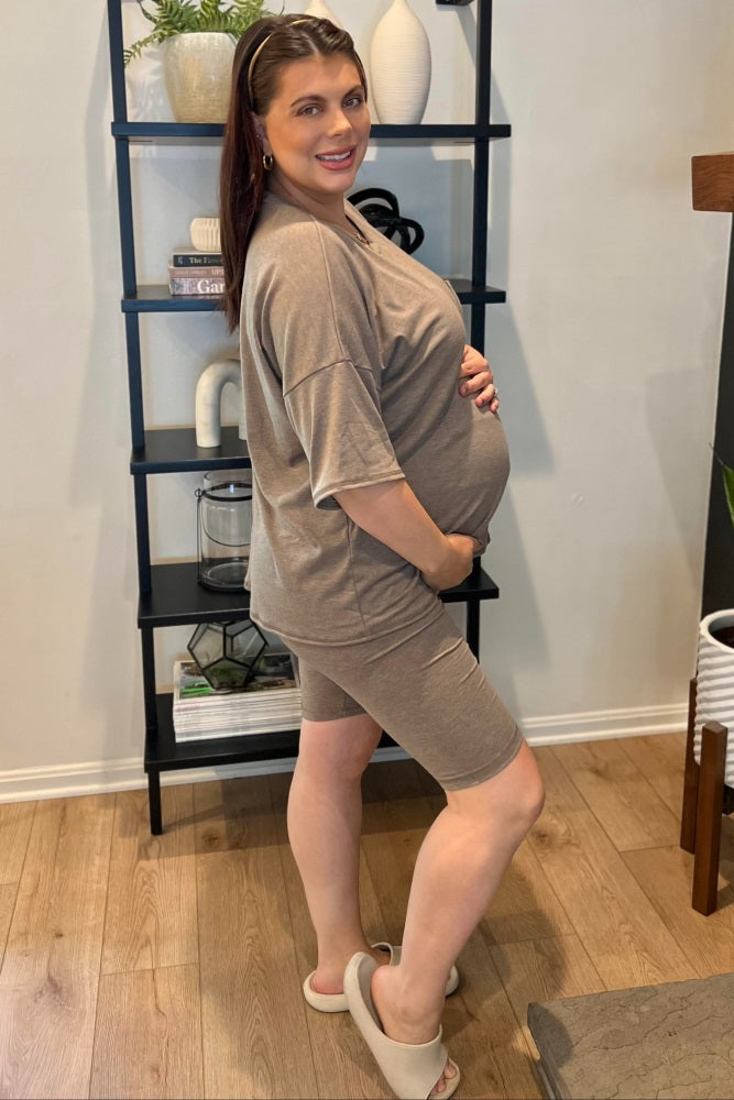 woman wearing a taupe maternity short sleeve top and matching biker shorts, cradling her baby bump