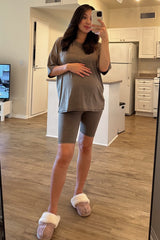woman wearing a grey maternity top and grey bike shorts, holding her baby bump in a home setting