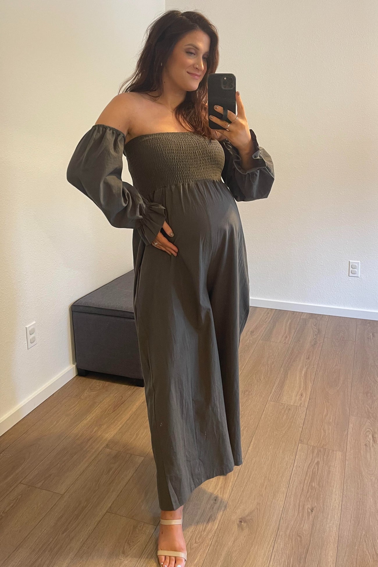 Pregnant woman in olive green off-the-shoulder maternity jumpsuit taking a mirror selfie