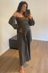 Pregnant woman in olive green off-the-shoulder maternity jumpsuit taking a mirror selfie